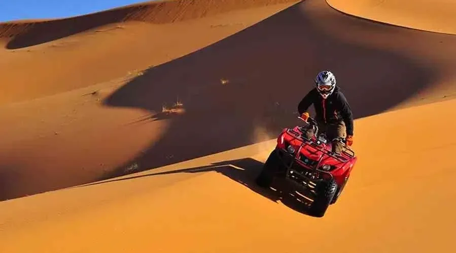 A man riding an ATV through the desert during the Marrakech to Fes Desert Tour, with sand dunes in the background.