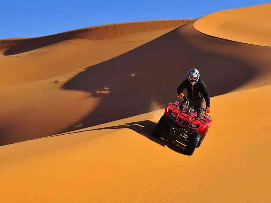 A man riding an ATV through the desert during the Marrakech to Fes Desert Tour, with sand dunes in the background.