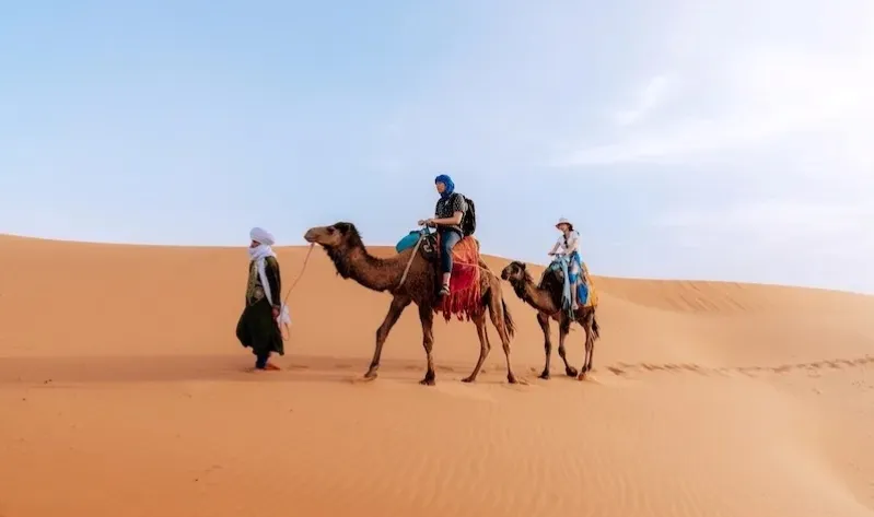 Three people riding camels across a vast desert landscape, showcasing a Luxury Tours Morocco experience.