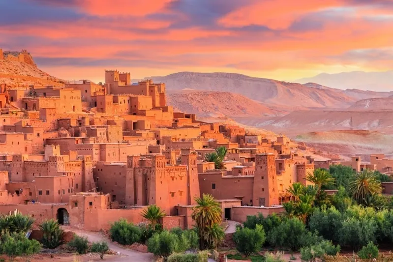 Sunset over the city of Atdhe, Morocco, showcasing vibrant colors and silhouettes of buildings against the evening sky.