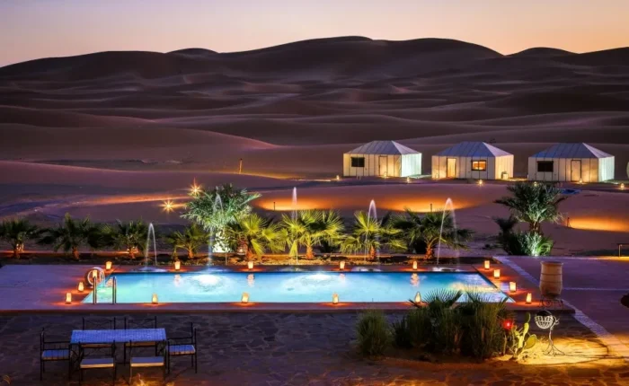 A serene pool in the desert, adorned with lights and a tent, highlighting the luxury of Morocco Tours.