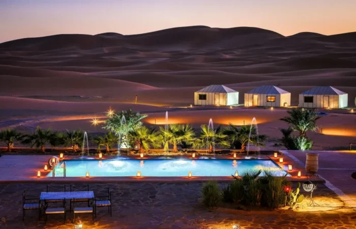 A serene pool in the desert, adorned with lights and a tent, highlighting the luxury of Morocco Tours.
