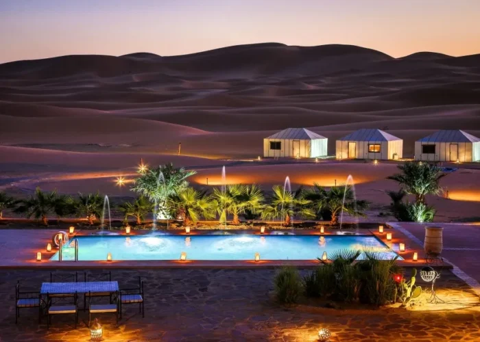 A serene pool in the desert, adorned with lights and a tent, highlighting the luxury of Morocco Tours.