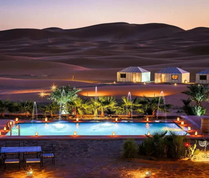 A serene pool in the desert, adorned with lights and a tent, highlighting the luxury of Morocco Tours.