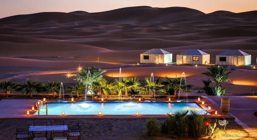 A serene pool in the desert, adorned with lights and a tent, highlighting the luxury of Morocco Tours.
