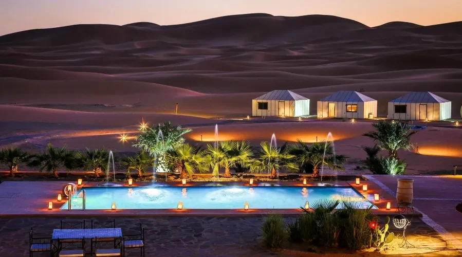 A serene pool in the desert, adorned with lights and a tent, highlighting the luxury of Morocco Tours.