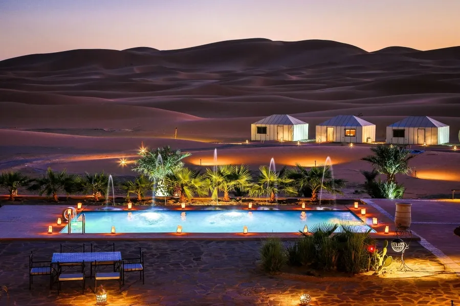 A serene pool in the desert, adorned with lights and a tent, highlighting the luxury of Morocco Tours.