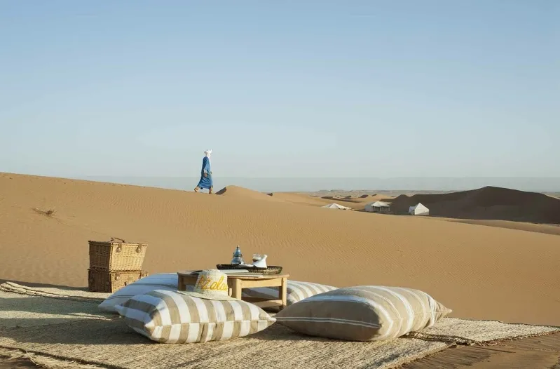 A picnic table and chairs set in the desert at a luxury camp in Merzouga, Morocco, surrounded by sandy dunes.