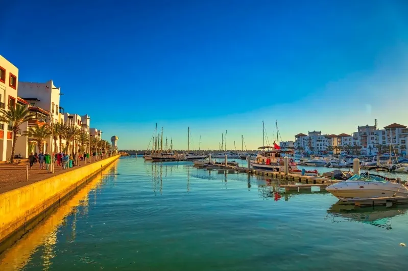 The marina at Agadir , with various boats docked and a backdrop of the city and mountains.