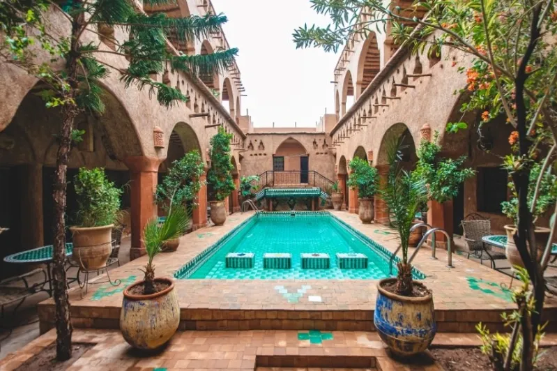 A serene pool in the courtyard of a luxurious old building in Morocco, surrounded by elegant architecture and greenery.