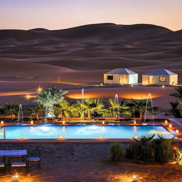 A luxurious desert pool at dusk, surrounded by a tent and soft lights, showcasing the beauty of Merzouga camp.