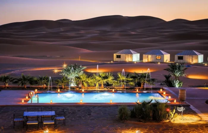 A luxurious desert pool at dusk, surrounded by a tent and soft lights, showcasing the beauty of Merzouga camp.