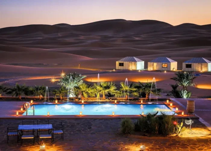 A luxurious desert pool at dusk, surrounded by a tent and soft lights, showcasing the beauty of Merzouga camp.