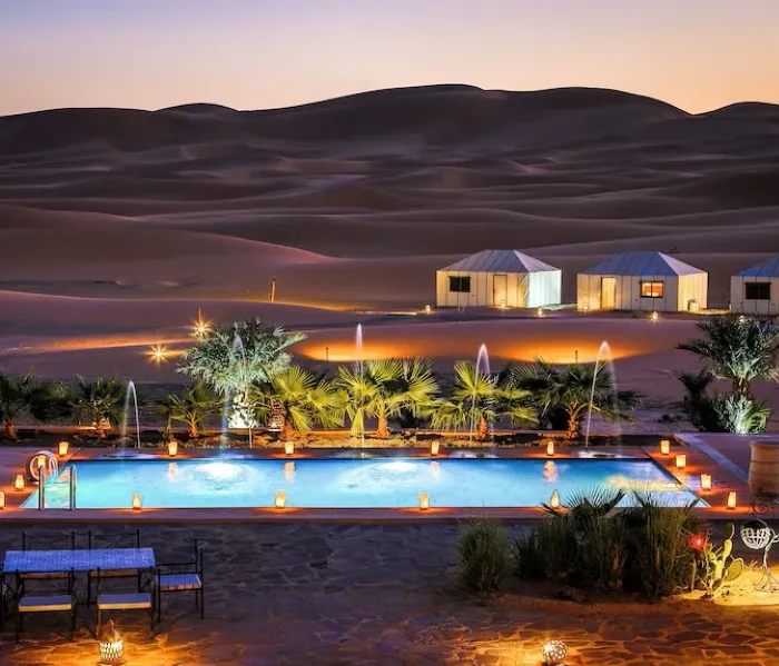 A luxurious desert pool at dusk, surrounded by a tent and soft lights, showcasing the beauty of Merzouga camp.