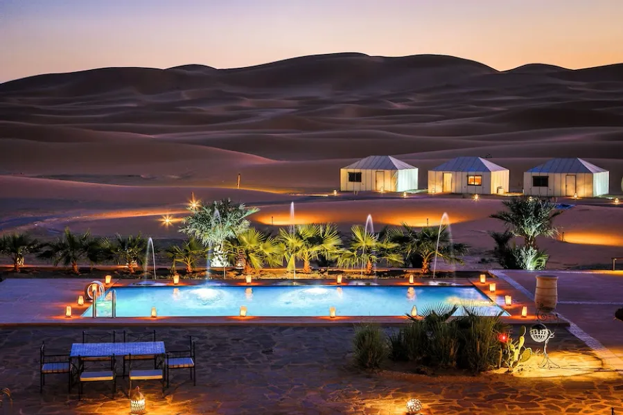 A luxurious desert pool at dusk, surrounded by a tent and soft lights, showcasing the beauty of Merzouga camp.